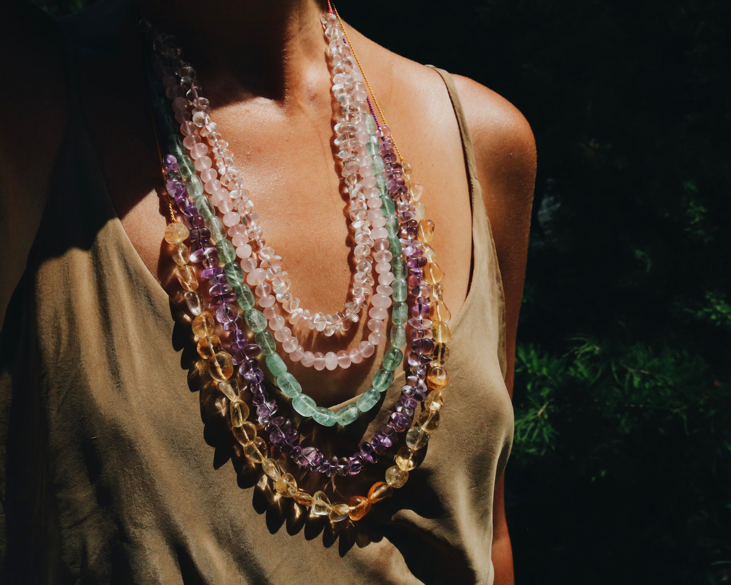 Multicolored natural stone adjustable beaded necklaces layered on a person with a dark background