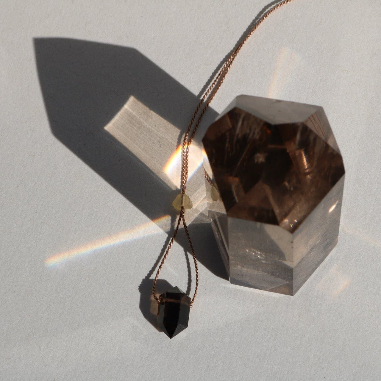 Smoky Quartz double point pendant on a silk cord with crystal and shadow in natural light on a light background