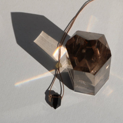 Smoky Quartz double point pendant on a silk cord with crystal and shadow in natural light on a light background